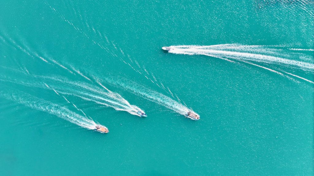 Aerial view of four speedboats creating dynamic trails on turquoise water.
